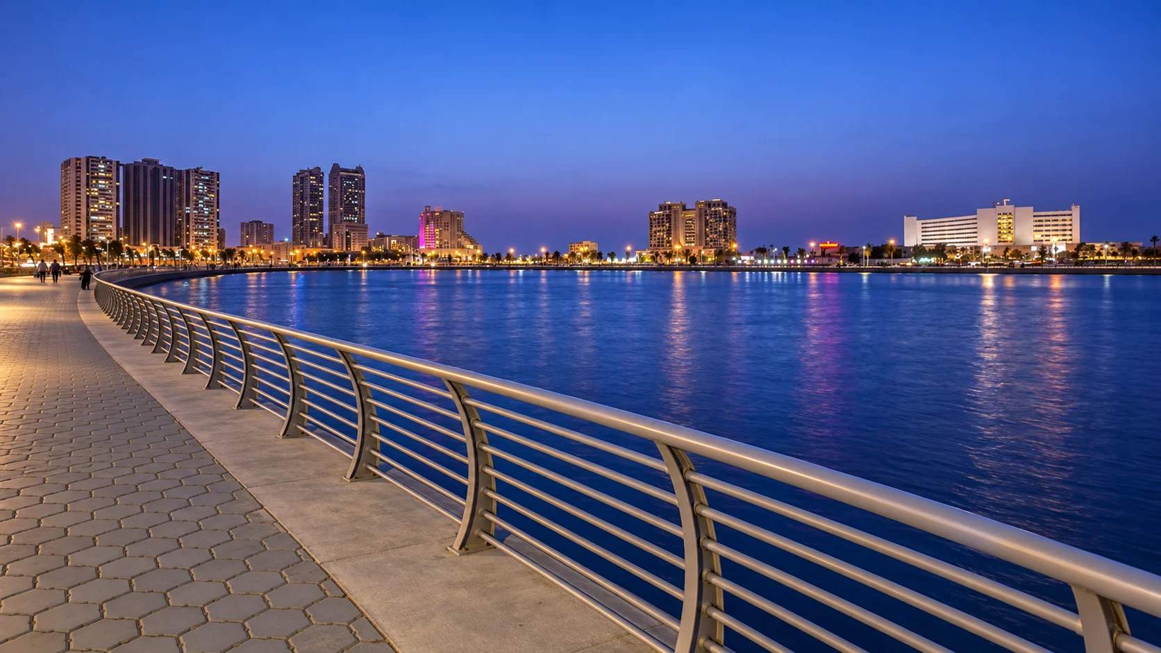 Изогнутая прогулочная дорожка у воды Ajman Marina в синих сумерках