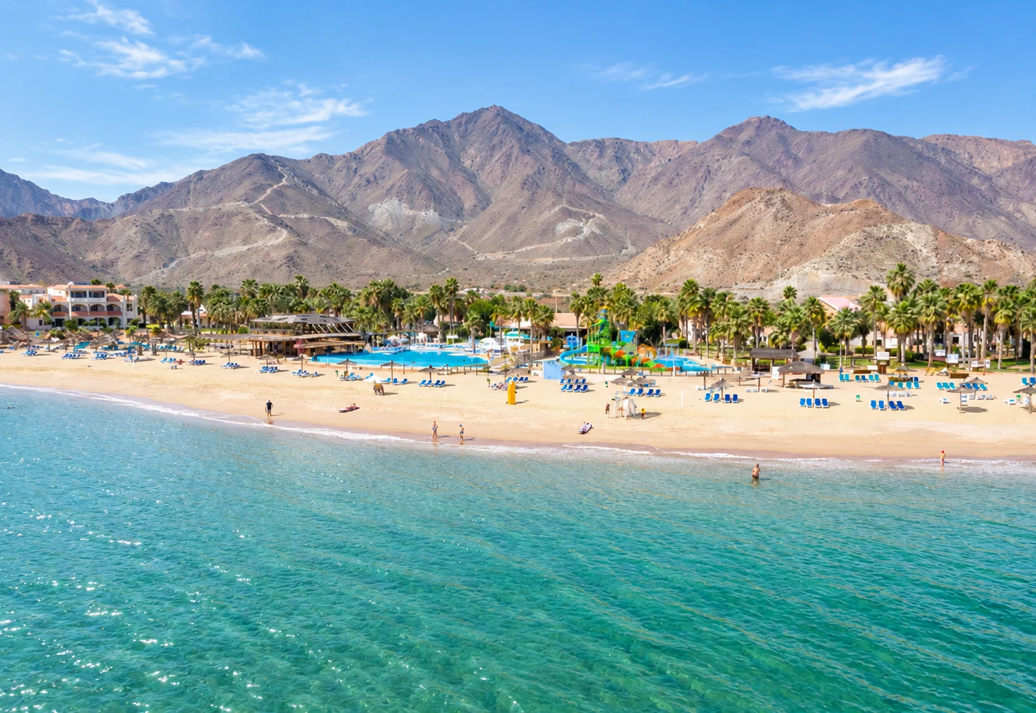 Пляж Sandy Beach, низкие здания, пальмы и горы за ними