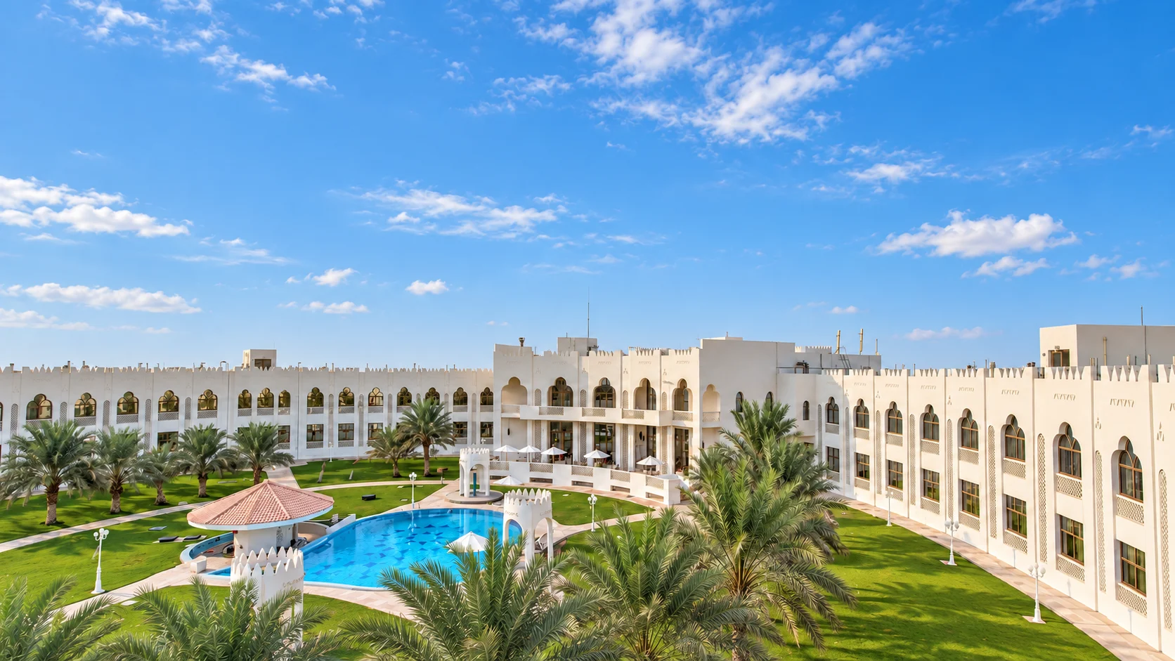 Белые аркады Liwa Hotel вокруг двора с пальмами и бассейном