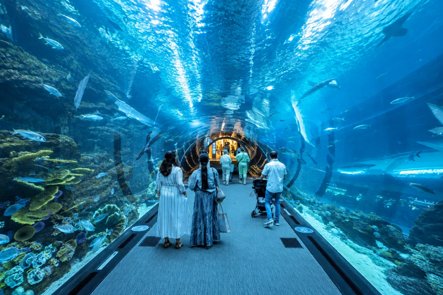 Посетители идут по синему тоннелю Dubai Aquarium под прозрачным сводом