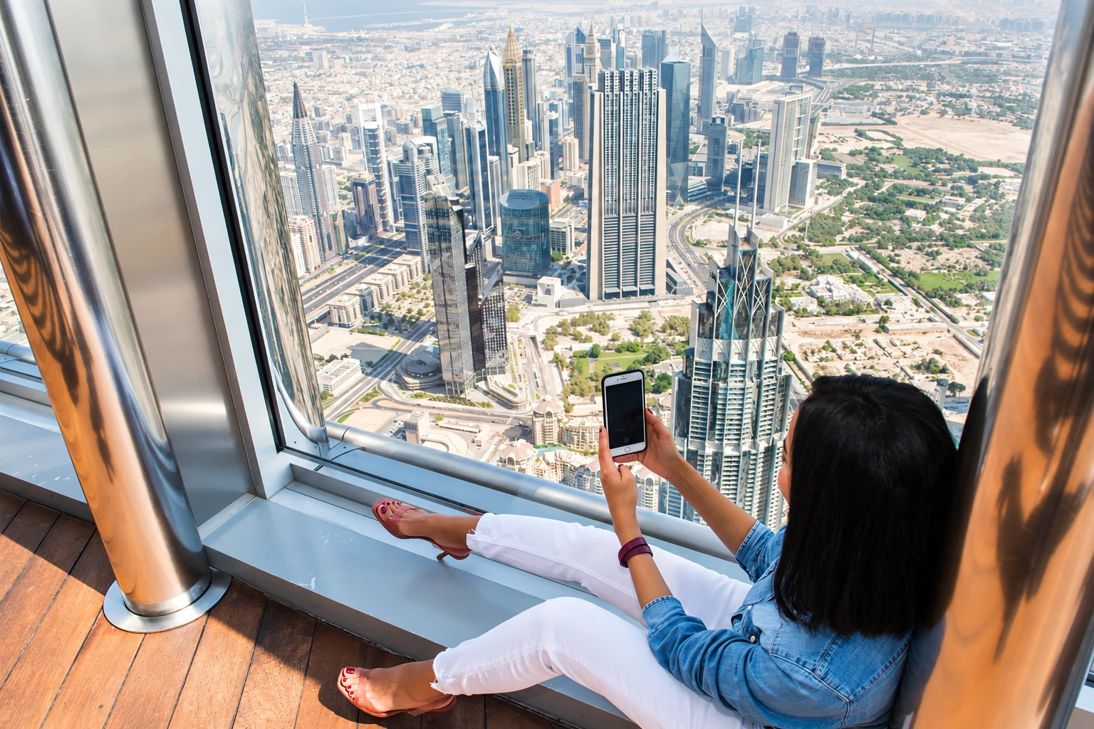 Посетительница фотографирует панораму Дубая через стекло на площадке At the Top