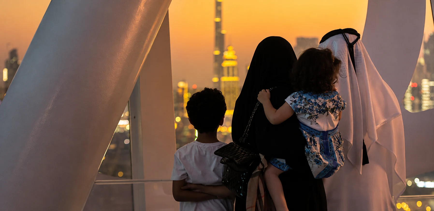 Семья у окна Dubai Frame смотрит на вечерний город