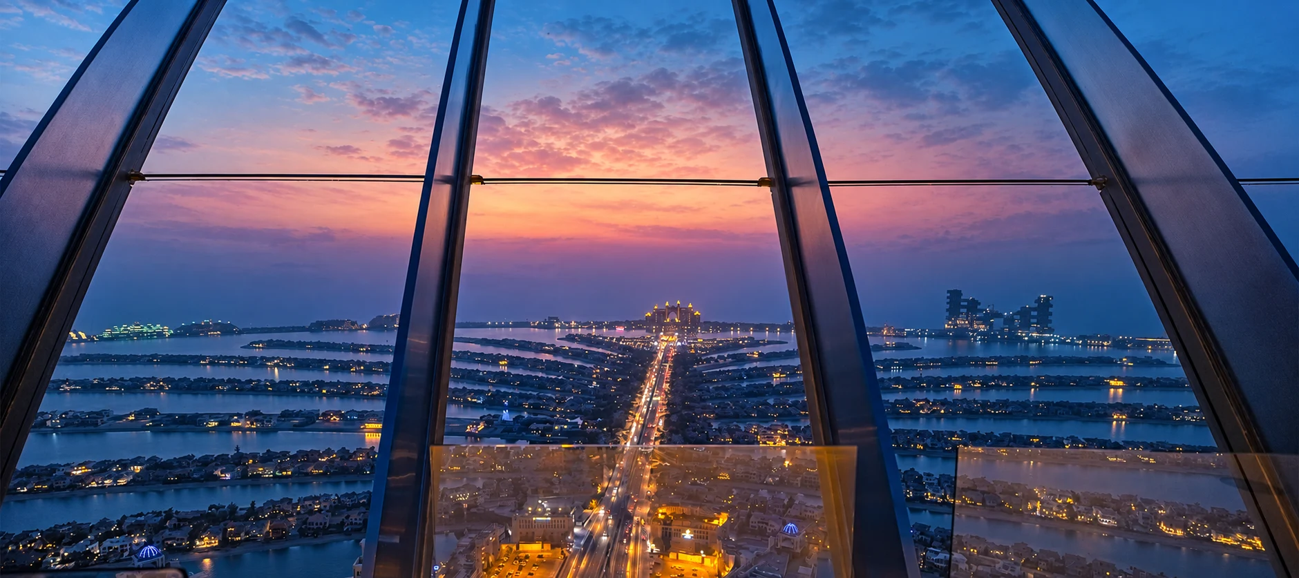 Вид через наклонные стеклянные панели The View на огни Пальмы в сумерках